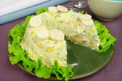 Maionese de batata com palmito em um prato na cor verde com folhas de alface em torno em uma mesa na cor marrom